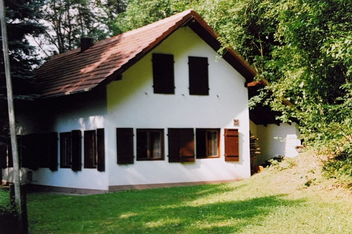 Historisches Farbfoto des Clubheims mit rotem Ziegeldach und dunklen Fensterläden zwischen Wiese und Bäumen