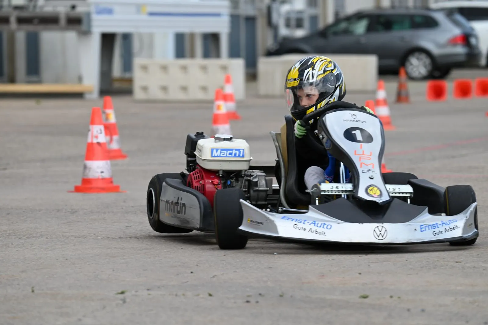 Nachwuchsfahrer mit gelbem Helm im Kart zwischen Pylonen